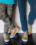 Load image into Gallery viewer, Two pairs of feet wearing colorful slip-on shoes against a white wall. - Thread Vision Client Spotlight, Goldfish Kiss
