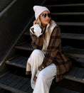 Load image into Gallery viewer, Person wearing a plaid coat, white pants, and a beanie sitting on stairs. - Thread Vision Spotlight, Hill x Sarah, Sarah Hill 
