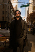 Load image into Gallery viewer, Man wearing sunglasses and a black hoodie on a city street with 'W 27 St' sign. - Thread Vision Spotlight, Kinda Handsome
