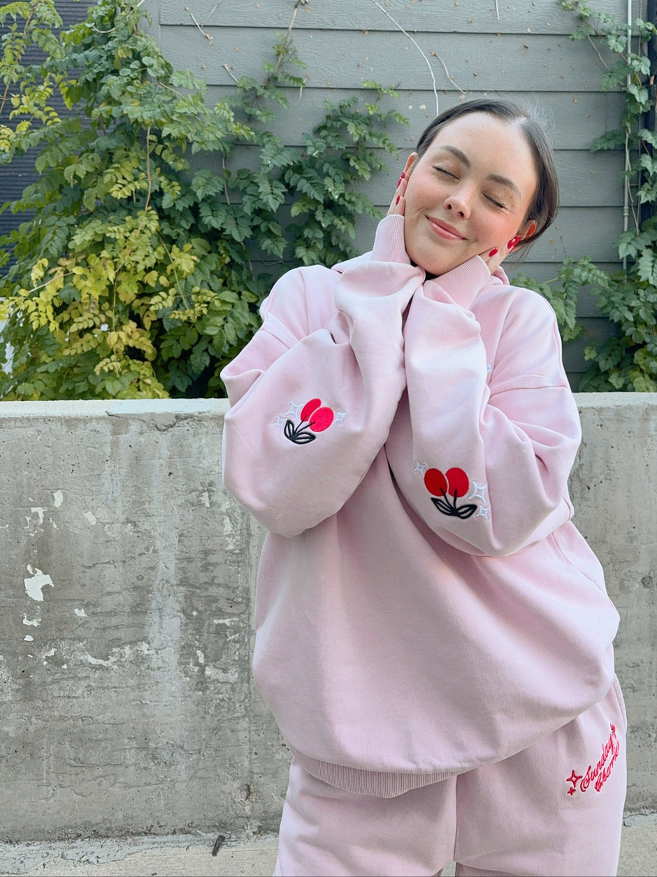 Person wearing a pink outfit with floral designs against a gray wall and greenery. - Thread Vision Client Spotlight, Sunday Cherries