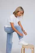 Load image into Gallery viewer, Woman in white t-shirt, blue jeans, and white sneakers sitting on a wooden stool against a plain background - Thread Vision Spotlight, Day 1 Fitness, Kaylee Rogers 
