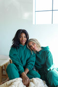 Load image into Gallery viewer, Two women in teal hoodies sitting together on a couch in a bright room. - Thread Vision Spotlight, Day 1 Fitness, Kaylee Rogers 
