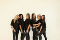 Load image into Gallery viewer, Group of six women in black outfits of cropped black t shirts and black leggings posing together against a beige background - Thread Vision Spotlight, Day 1 Fitness, Kaylee Rogers 
