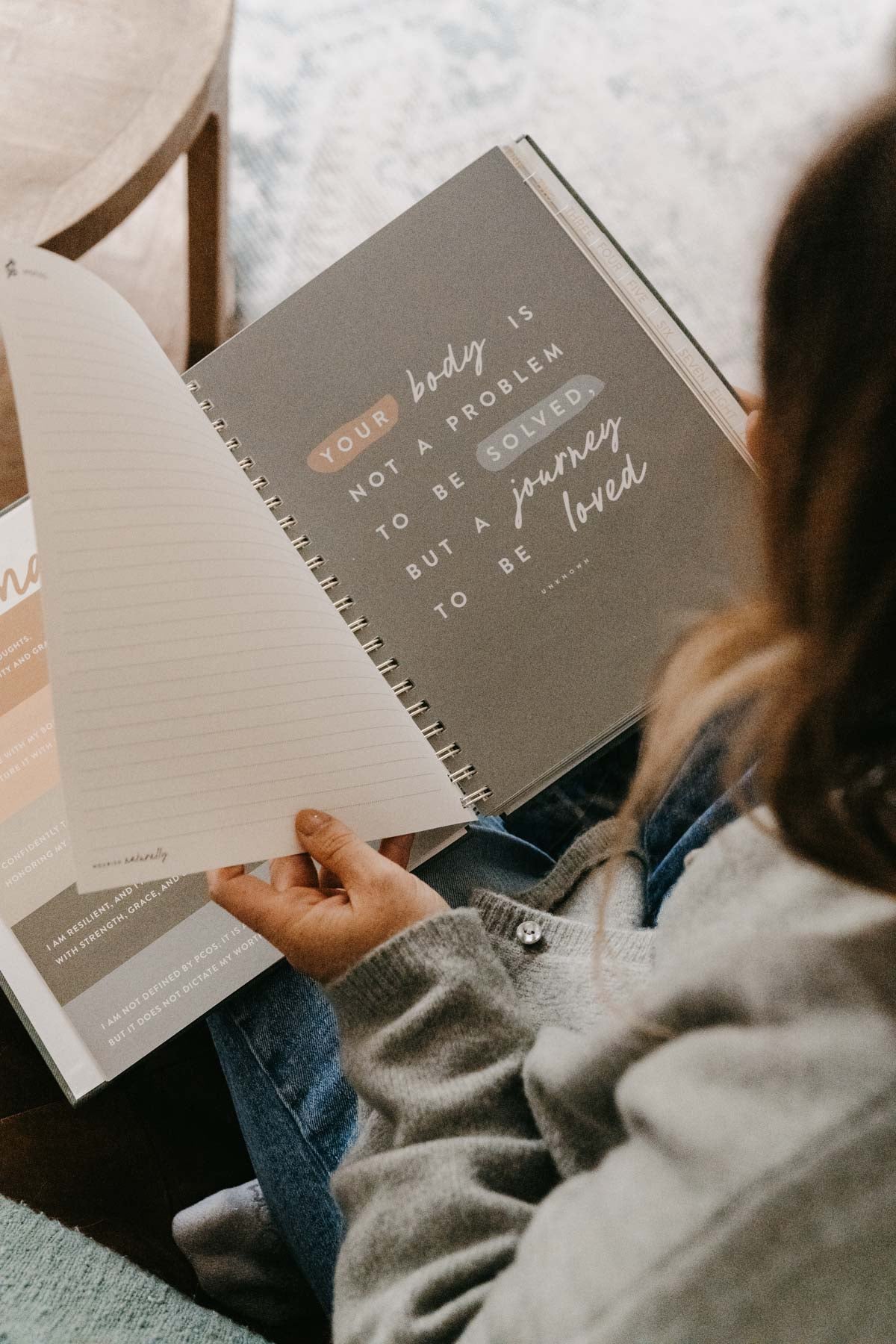 Person holding a notebook with motivational text, sitting by a window. - Thread Vision Spotlight, PCOS Planner