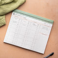 Load image into Gallery viewer, Weekly meal planner on a brown surface with a green cloth and pen - Thread Vision Spotlight, Oh Snap Macros
