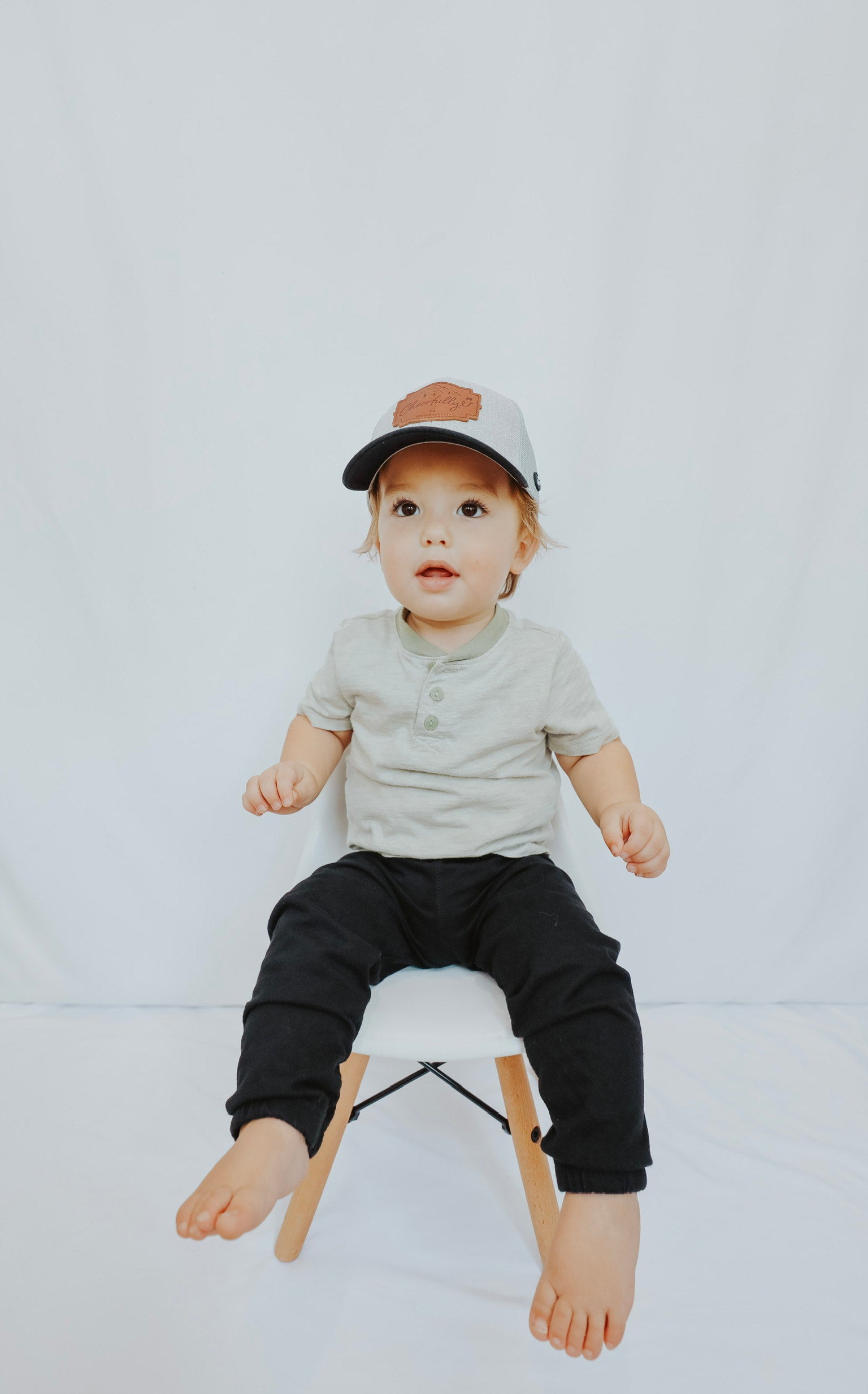 Child sitting on a stool wearing a cap and casual clothing against a plain background - Thread Vision Client Spotlight, Cheerfully U by Alyssa Webster 